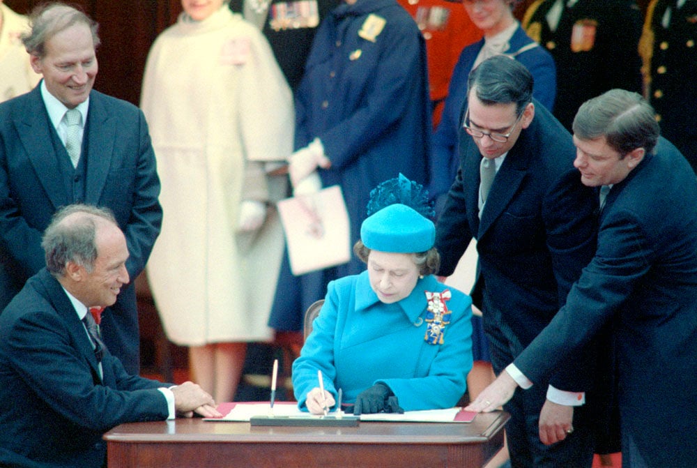1982 photo of Queen Elizabeth with then PM Pierre Elliot Trudeau signing Canada's Charter of Rights and Freedoms which Zionists are trying to kill to prevent protests of Israel's genocide of Palestinians