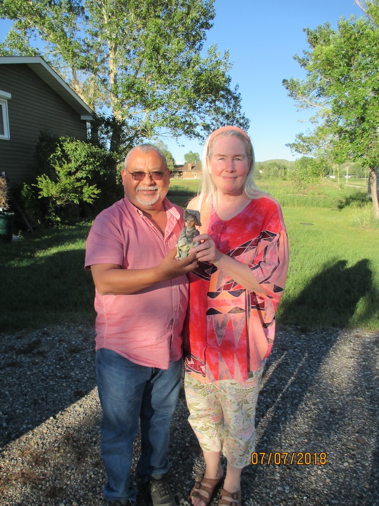 2018 photo of melo and jessica with rosebud in the background. they are holding the halloween witch jessica had in her chokecherries that melo loved and jessica gifted him on a hot summer day
