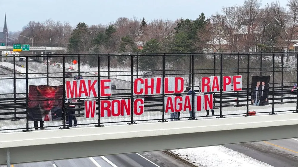 2026 photo of protest sign in cleveland on over pass which says "make child rape wrong again" with photo of Epstein with Trump to the right and photo of trump with devil horns to the left. A few protesters are seen behind the text and a 4 lane road is beneath it