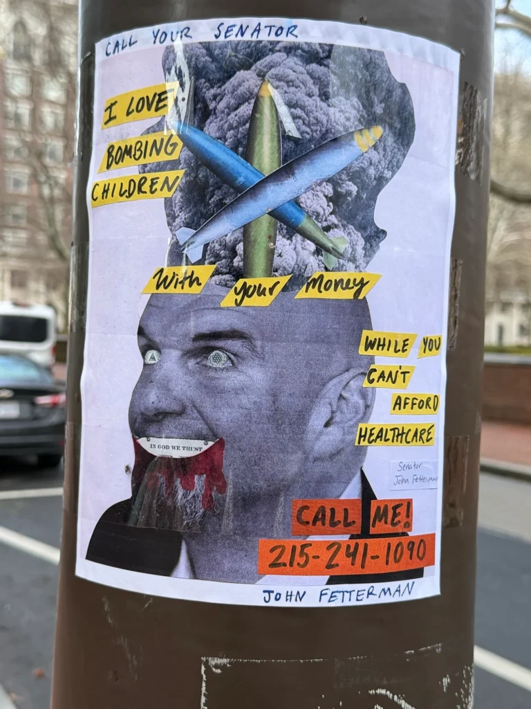 A flyer taped to a utility pole It features John Fetterman’s face with the eyes and mouth replaced by elements from American printed money , under the words “call your senator” and “I love bombing children with your money while you can’t afford healthcare “ and “call me” with his office number I assume
