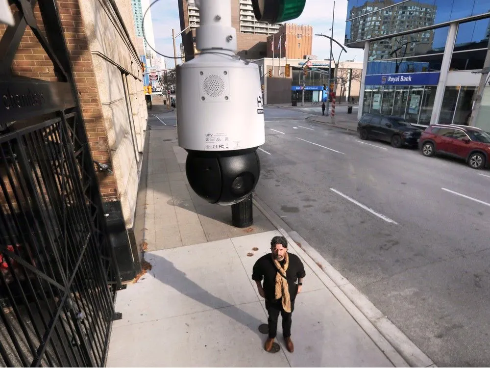 photo of man standing on sidewalk staring at Windsor's mass surveillance camera above him